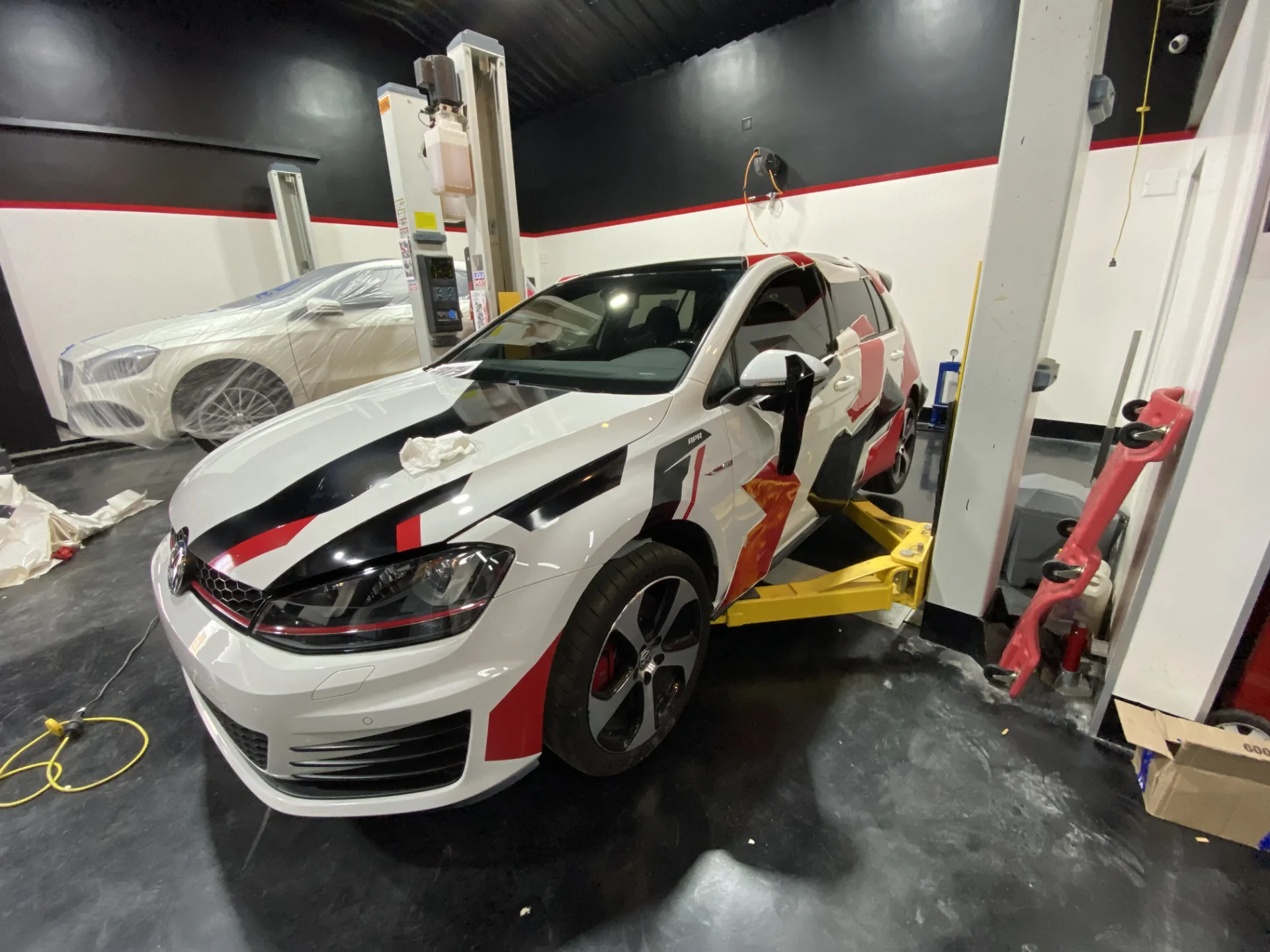 Volkswagen Golf GTI blanco con librea APR sobre elevador en taller